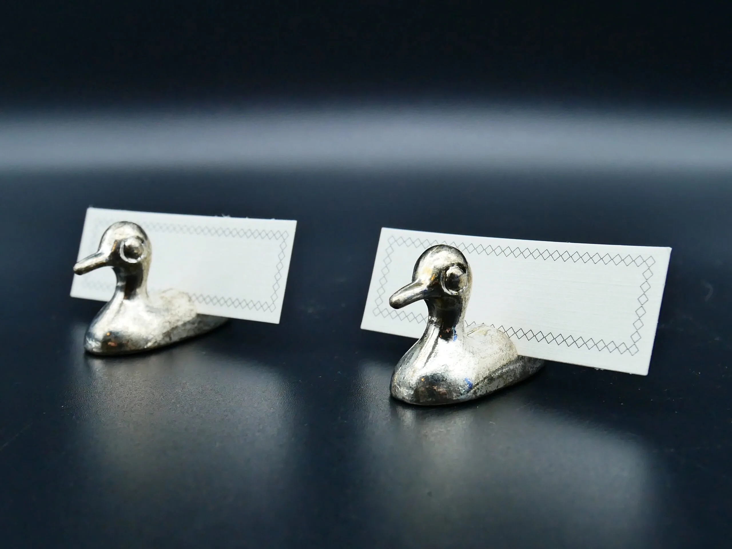 Pair of silver metal duck figurines holding blank place cards for elegant table settings