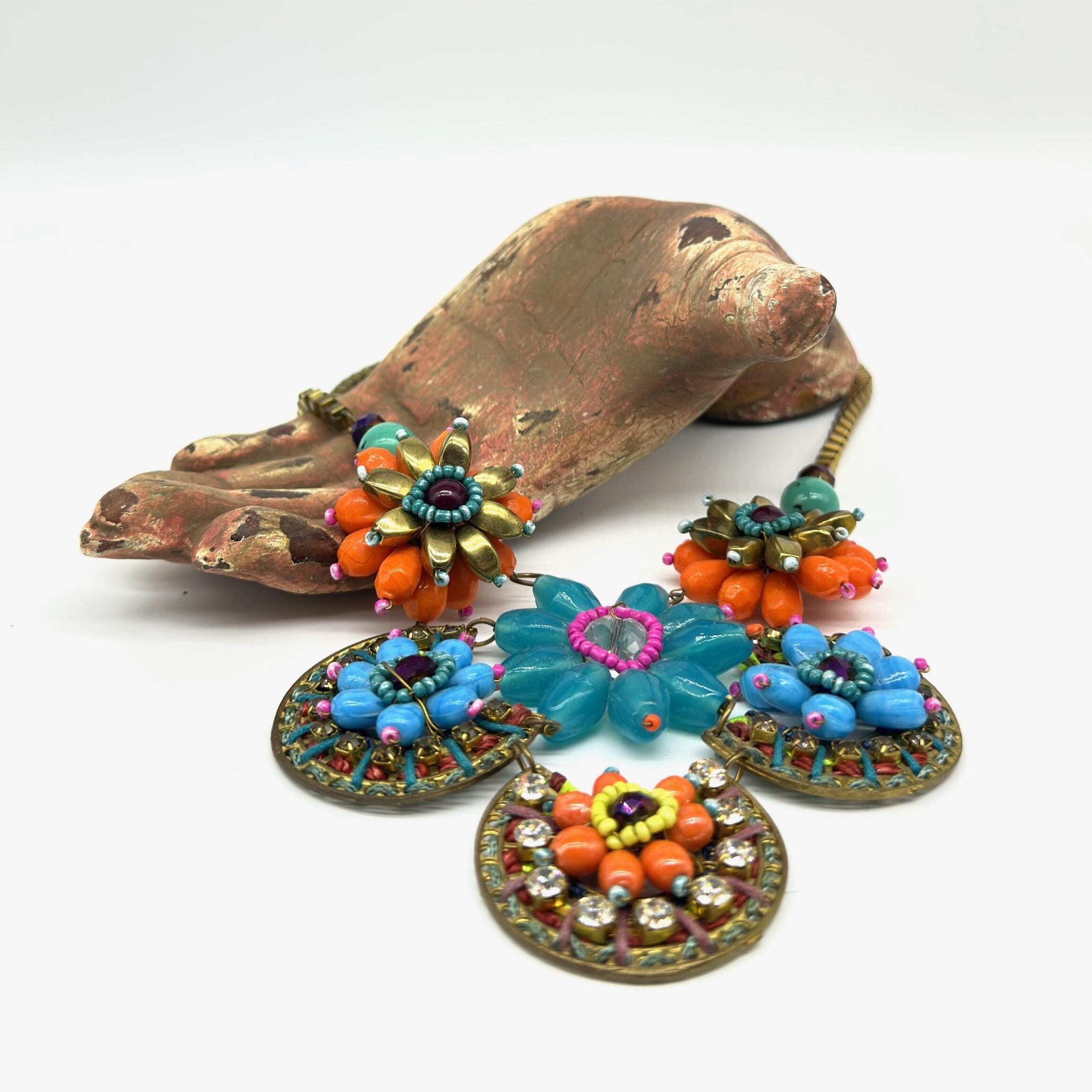 Adjustable boho necklace with layered beaded flowers in blue, coral, and jewel tones beside vintage brass sculptural accessor