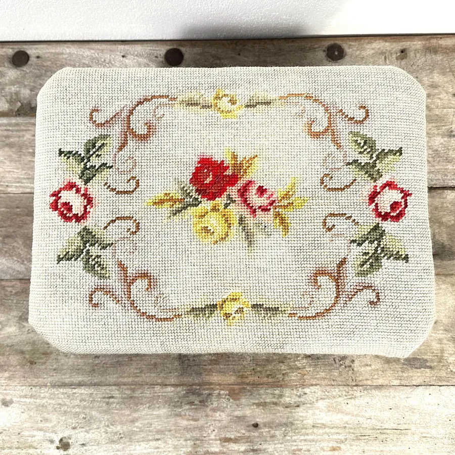 Angled rear view of footstool showing back leg structure, wood grain character, and complete embroidery coverage from behind