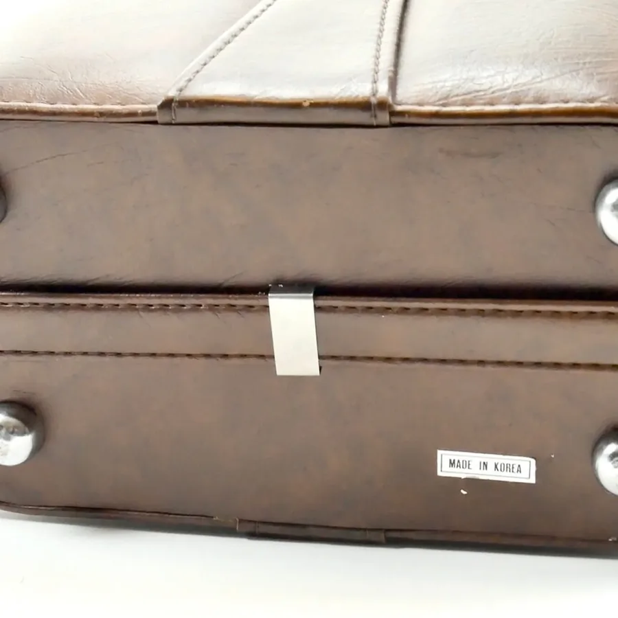 Bottom corner of camera bag showing brass hardware rivets, maker label, and weathered leather construction