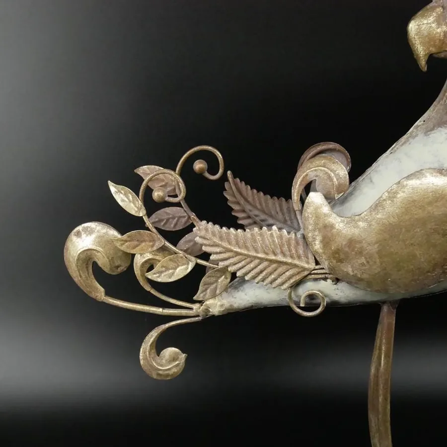 Close-up detail of metal parrot's ornamental tail feathers showing intricate scrollwork and warm metallic patina