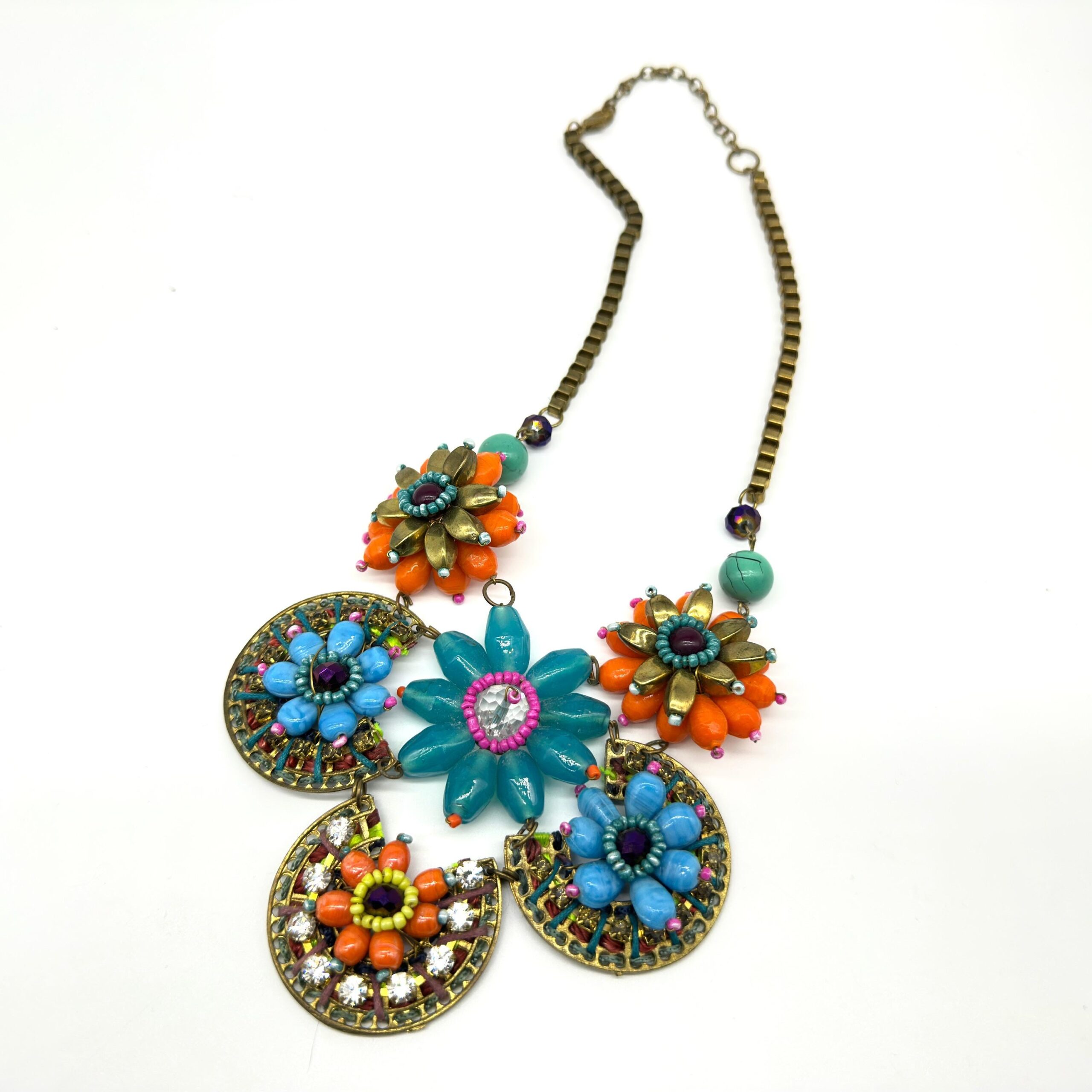 Flat lay of vintage floral statement necklace showing adjustable brass chain with five distinct beaded flower pendants in mul