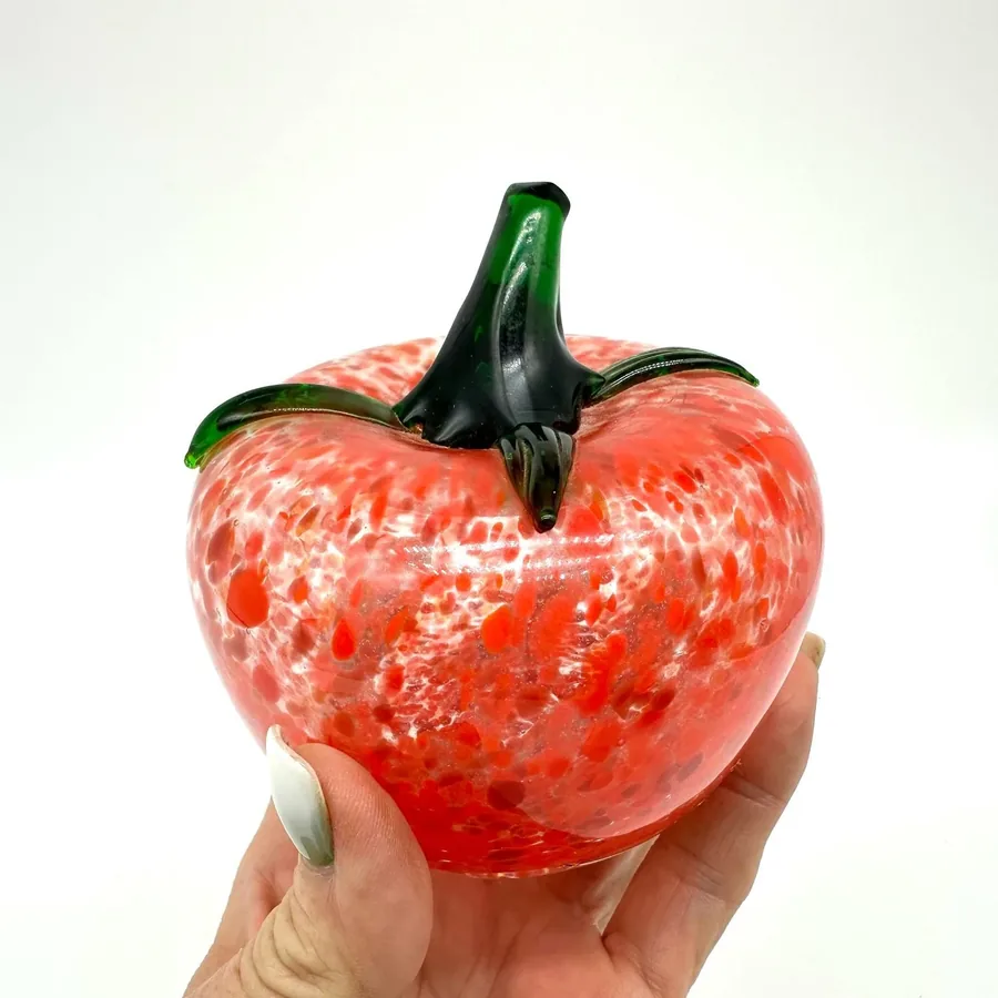 Glass tomato cradled in hand displaying smooth curved surface and white speckle pattern detail