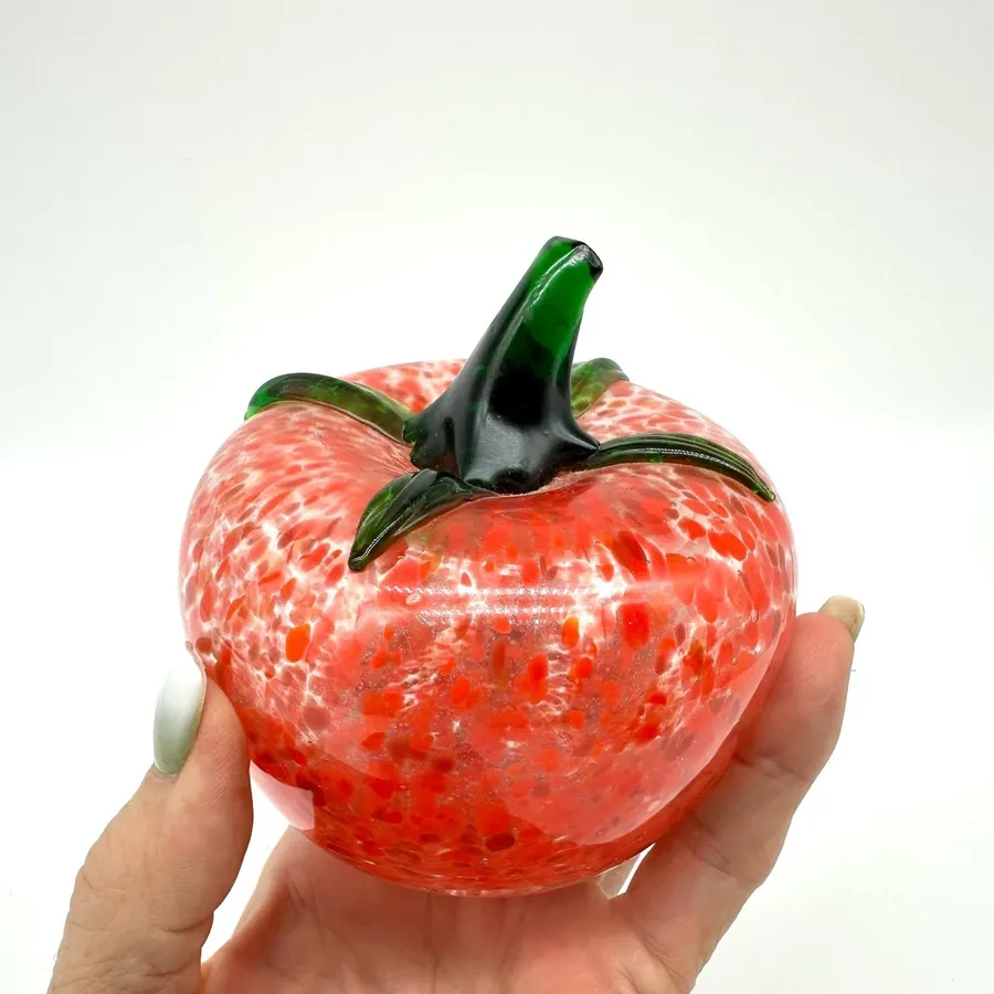 Hand cradling red speckled glass tomato showing dimensional form and green stem craftsmanship