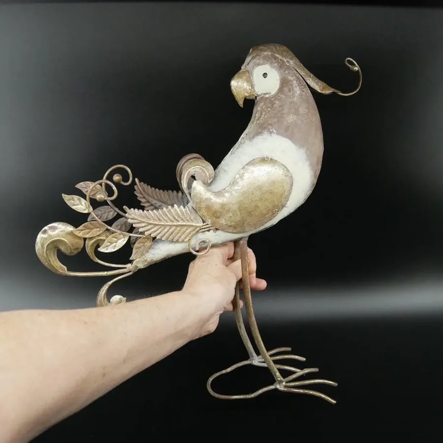 Metal parrot held aloft displaying full form with ornate tail spread, showcasing handcrafted quality and sculptural presence