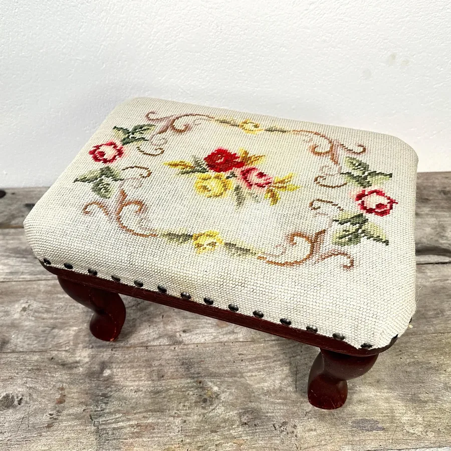 Needlepoint footstool side profile displaying wooden leg craftsmanship and embroidered textile detailing
