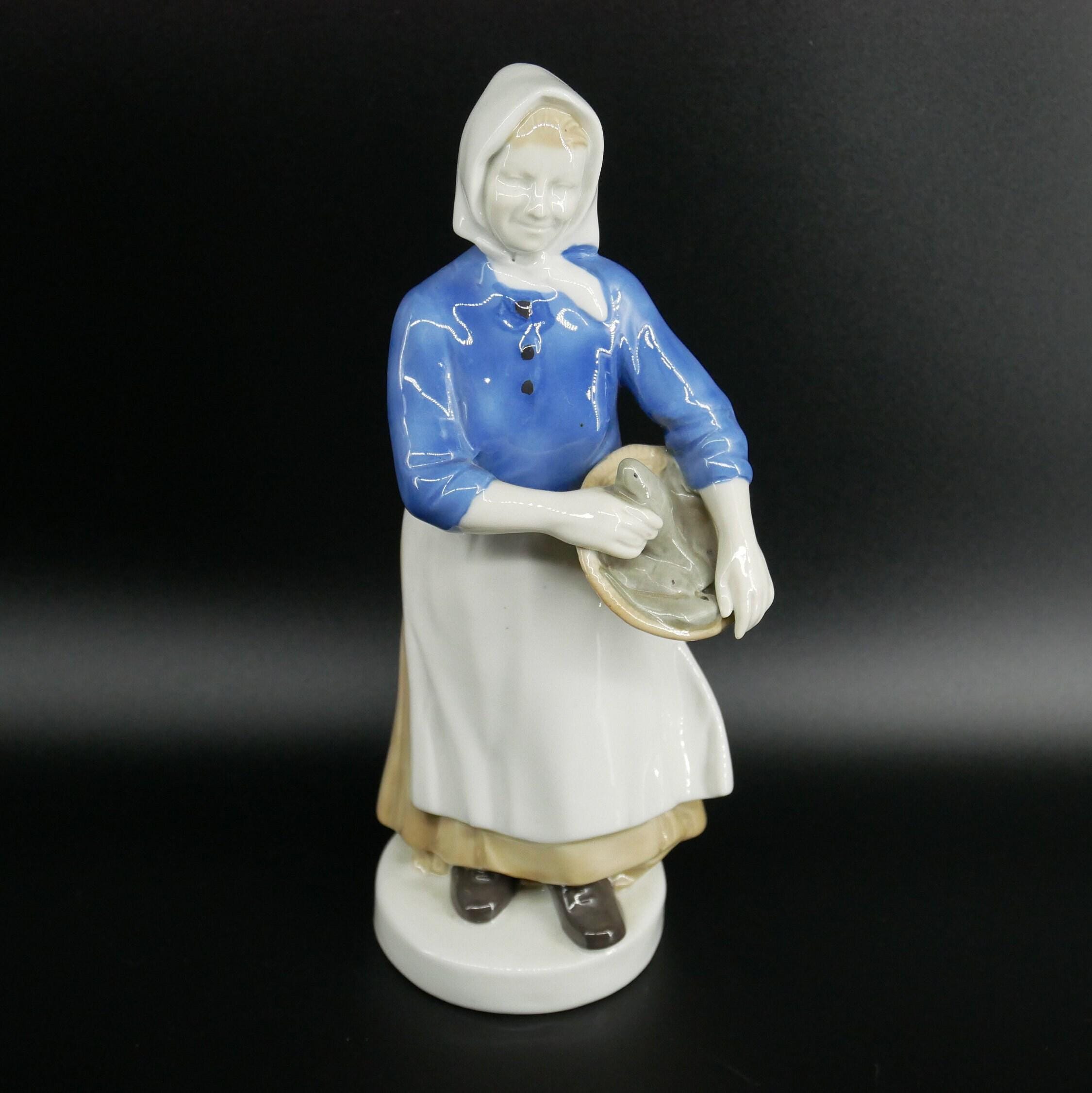 Porcelain fisherwoman figure holding basket, three-quarter view emphasizing painted blue garment and serene expression