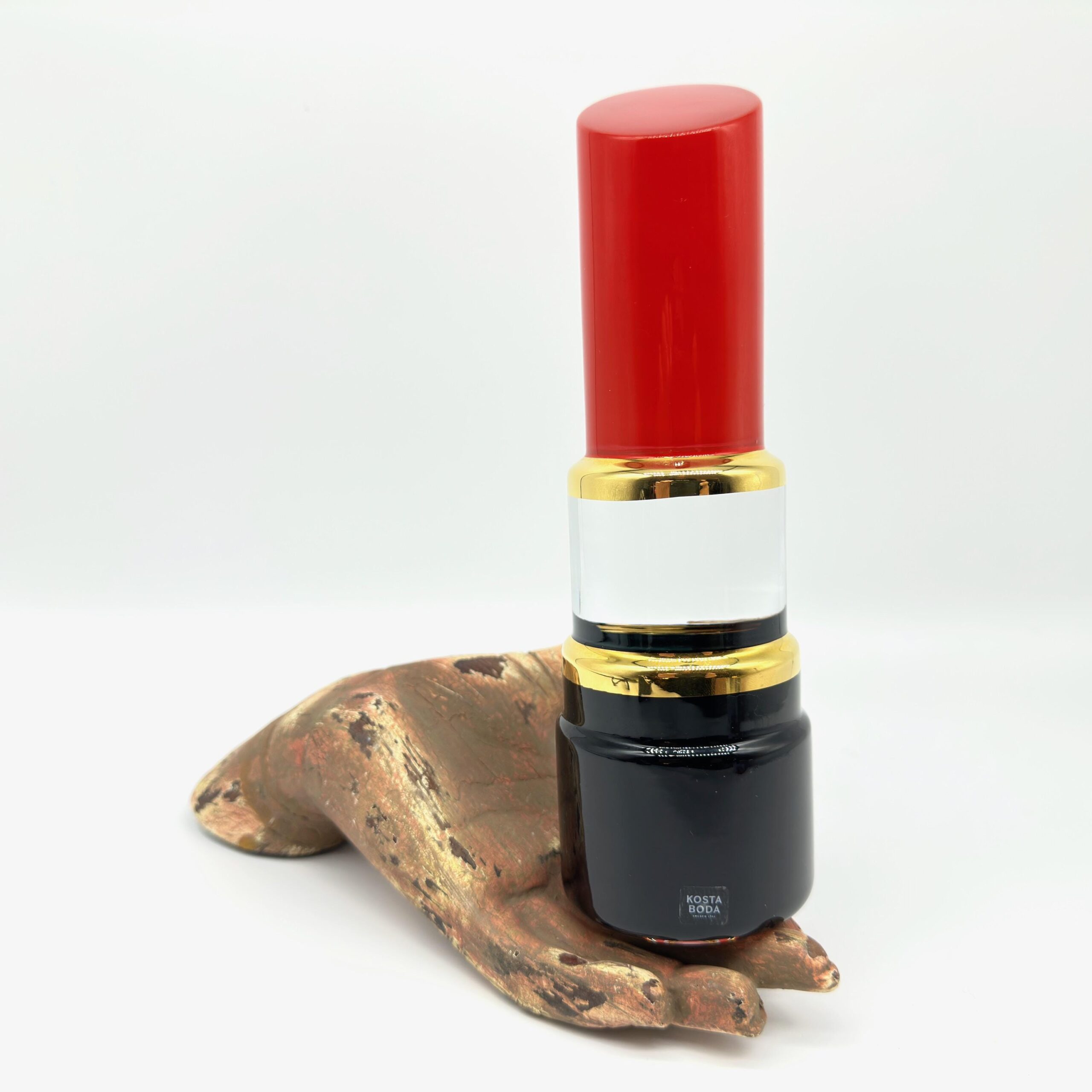 Red lipstick sculpture with bronze hand at three-quarter angle, complete view of sculptural ensemble and styling