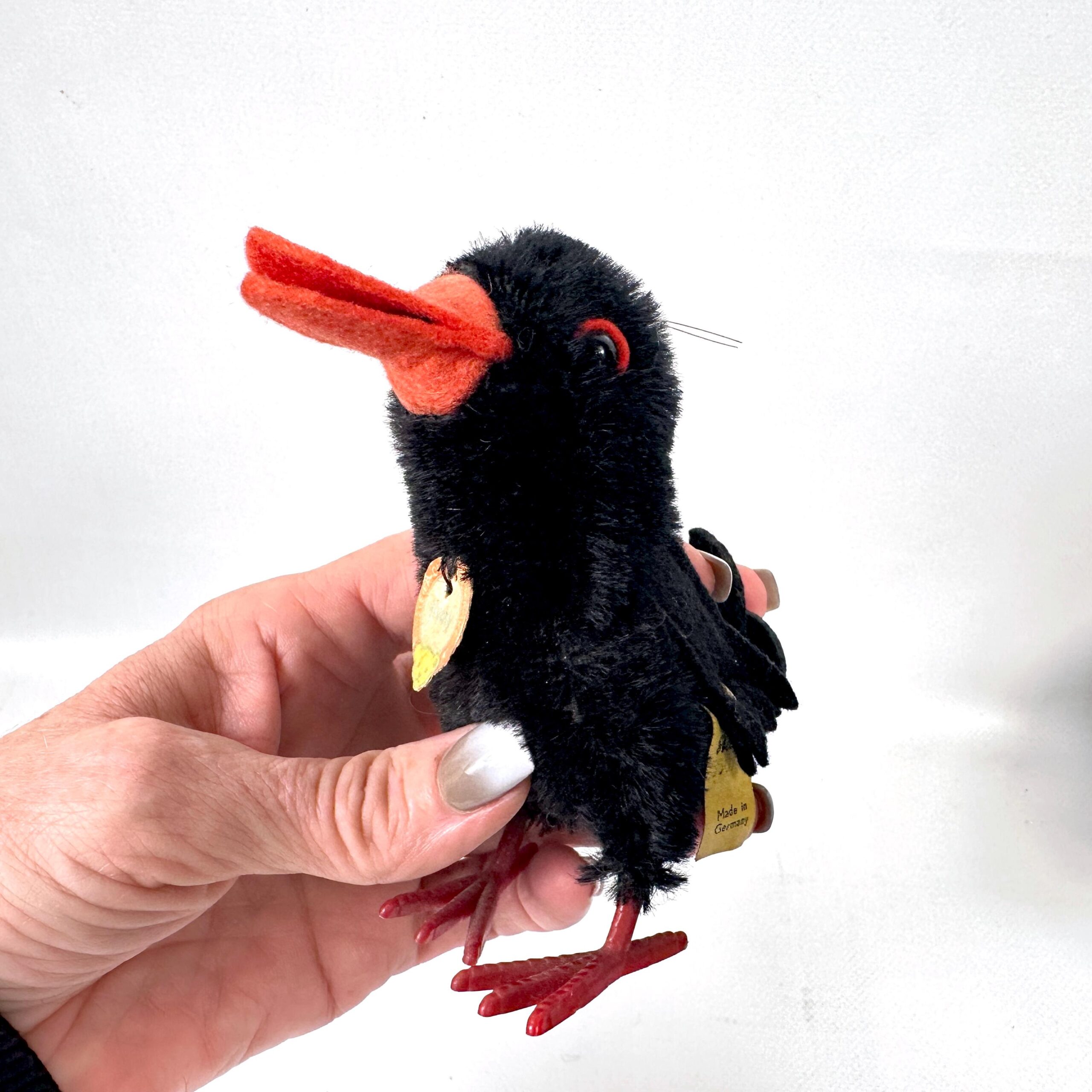 Single small vintage Steiff Hucky Bird in hand showing black mohair texture, orange beak detail, yellow belly patch, and auth