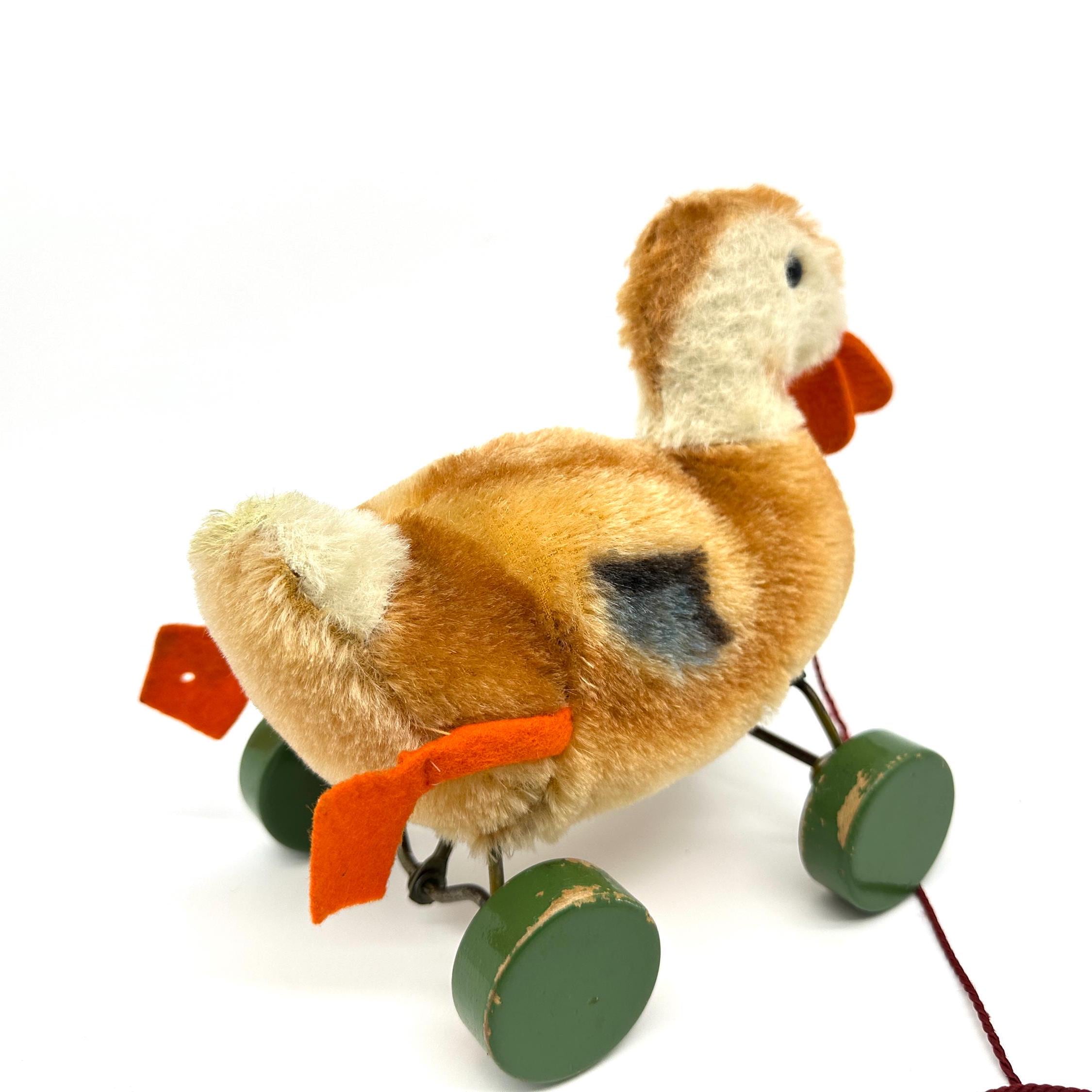 Steiff duck captured at dynamic angle showing mohair body, fabric ribbon detail, and wheeled pull mechanism together