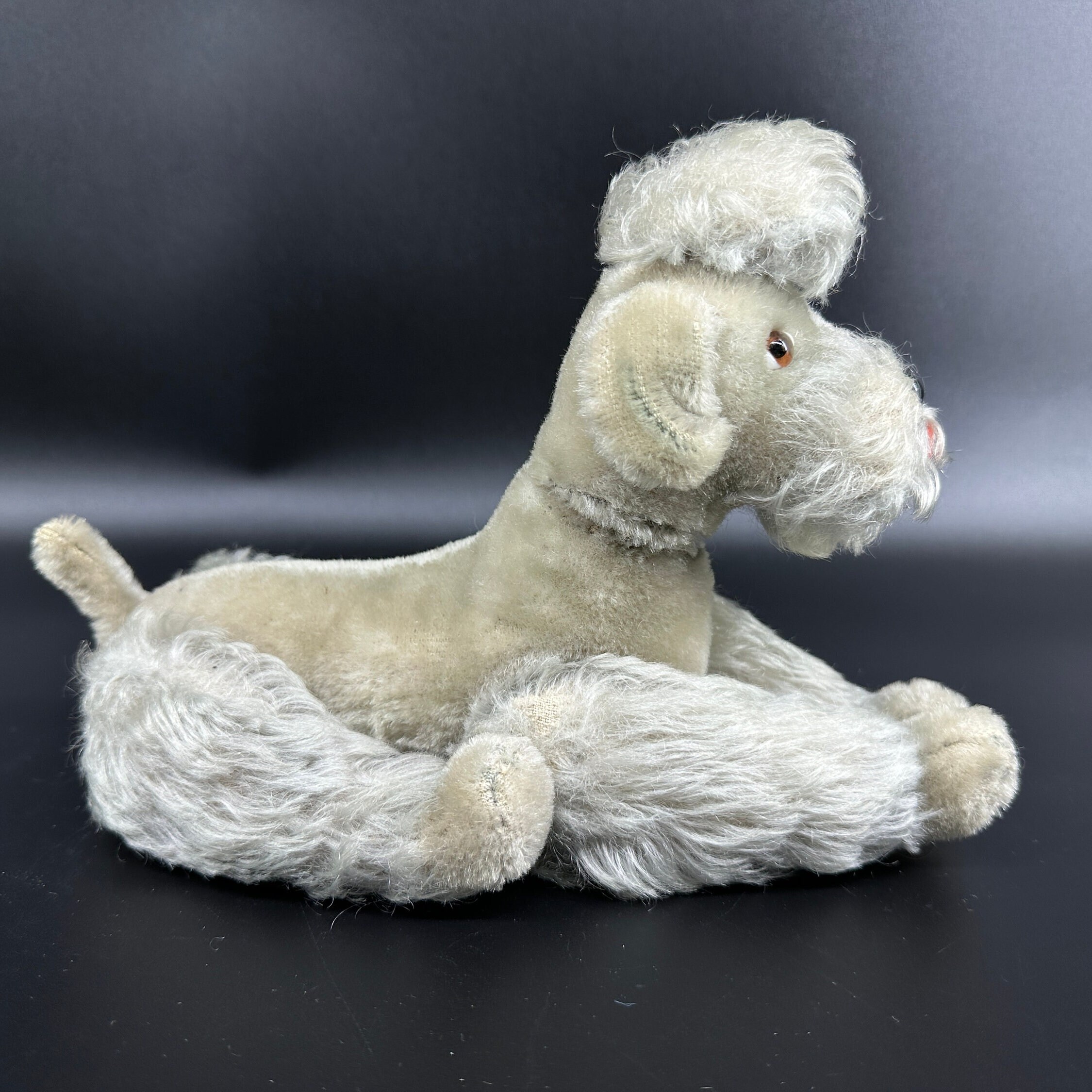 Steiff poodle in relaxed reclined position showing side profile of stretched body and fluffy texture