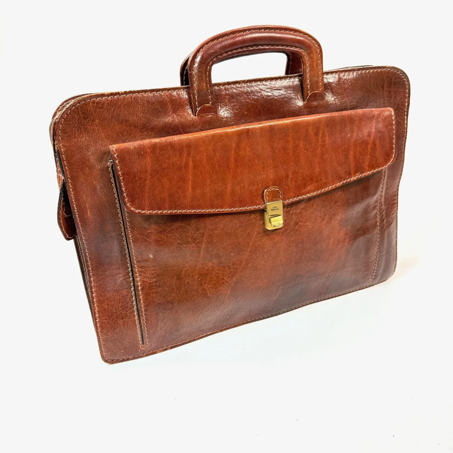 The Bridge vintage brown leather briefcase, full front view showing structured silhouette with brass clasp and dual handles