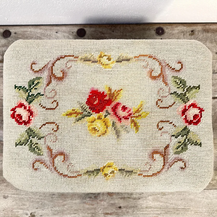 Three-quarter view of needlepoint footstool displaying frame silhouette and complete embroidered textile coverage