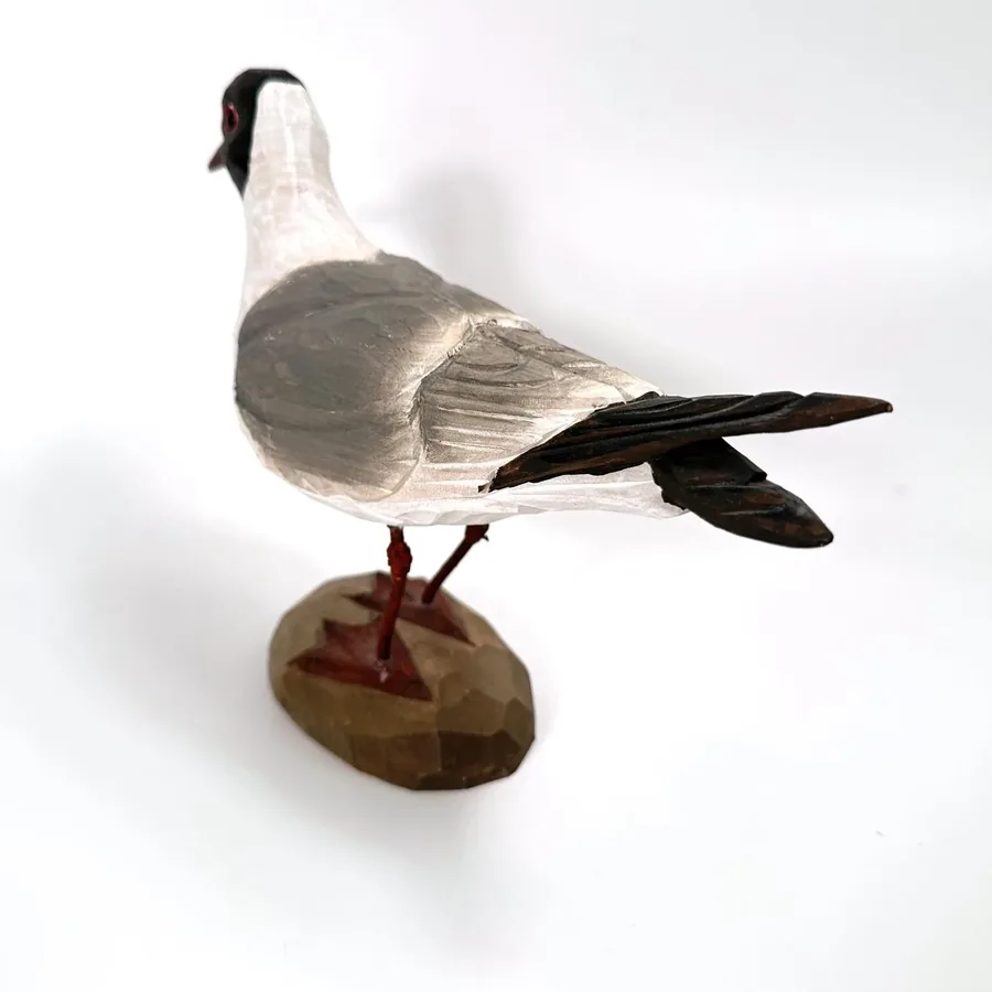 Three-quarter view of vintage seagull showing extended black wings, gray plumage, and resting stance on wooden base