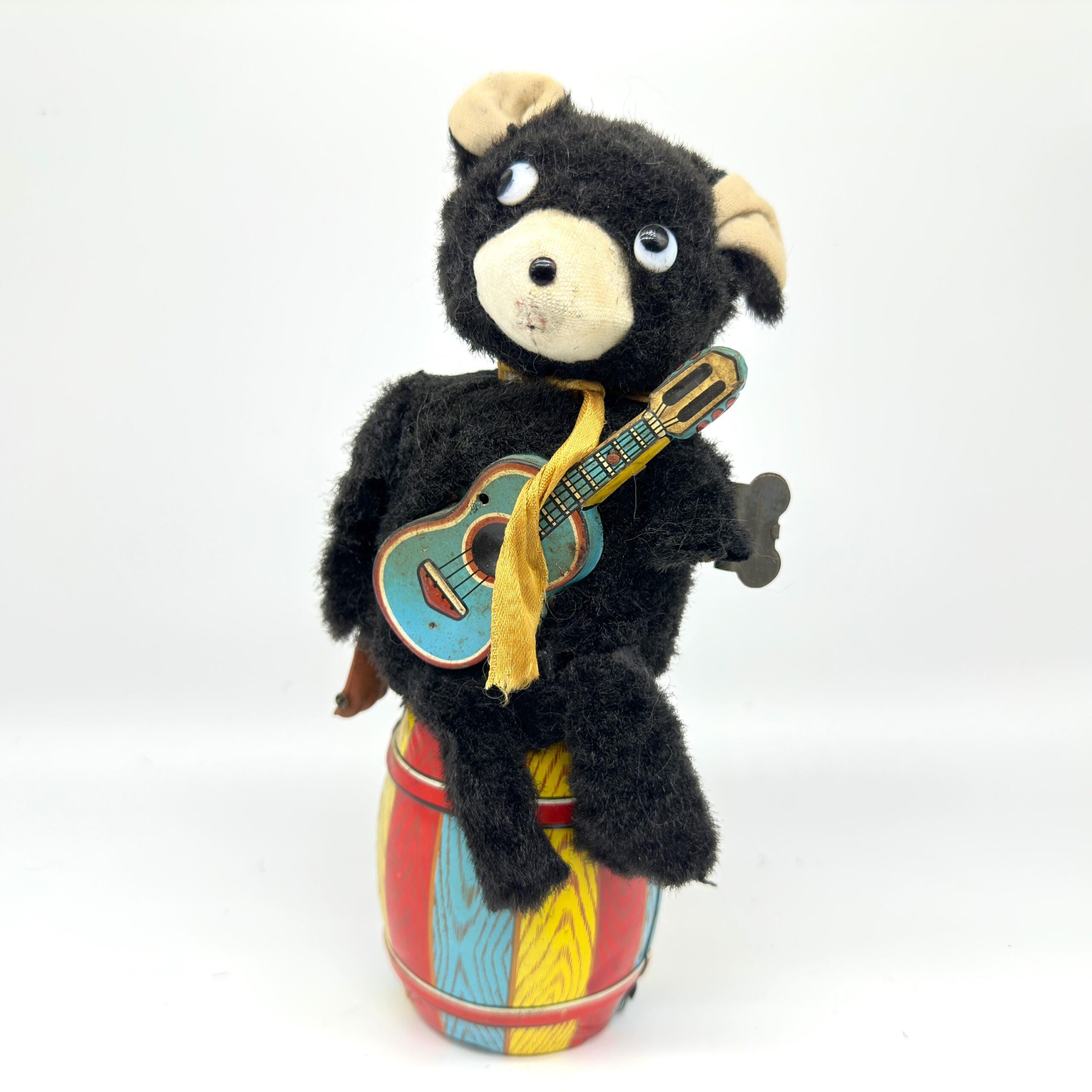 Vintage 1950s Nomura Jolly Guitarist bear with black plush fur, cream face, holding blue guitar, colorful striped base