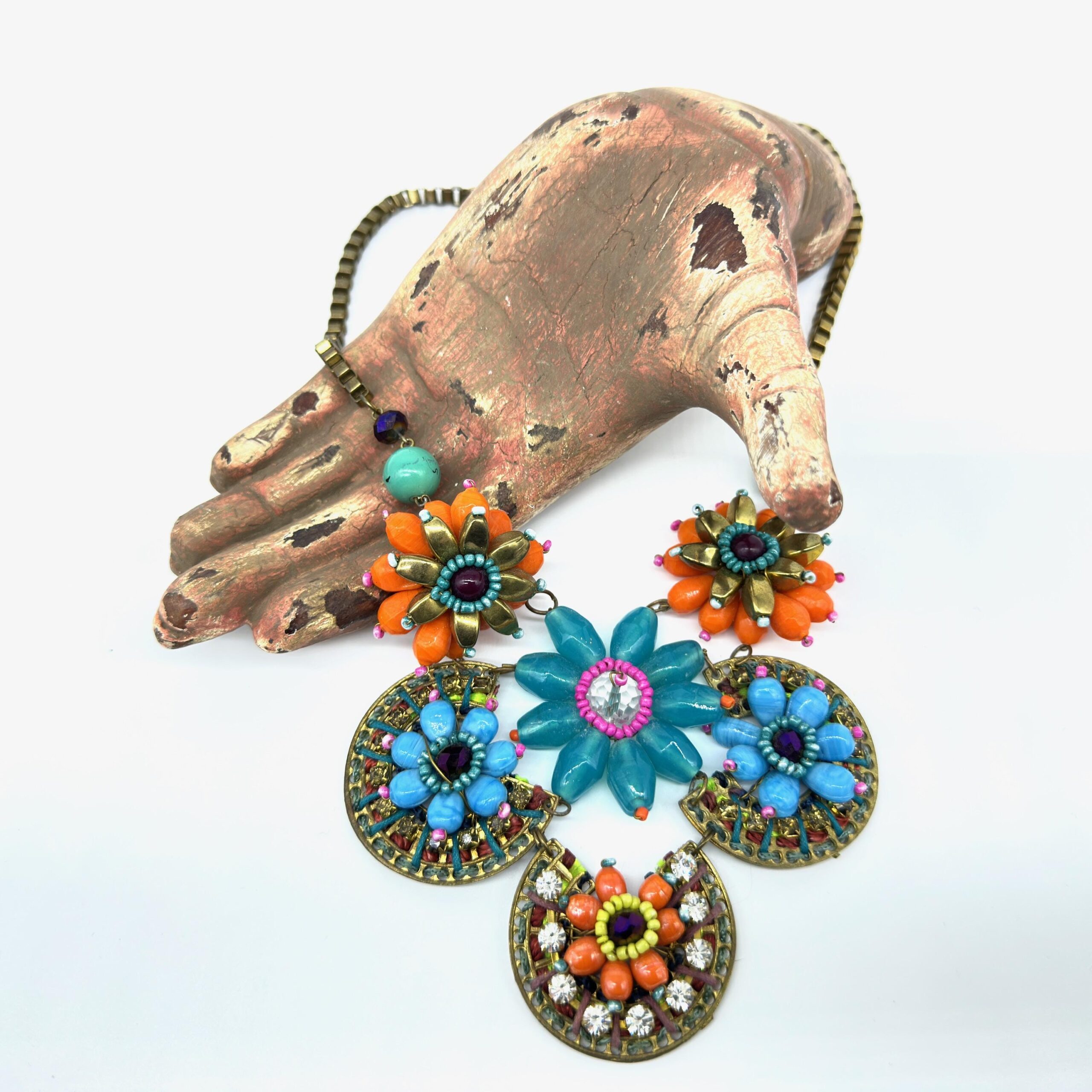 Vintage boho necklace with five beaded flowers in multicolor displayed alongside weathered brass sculptural hand collectible