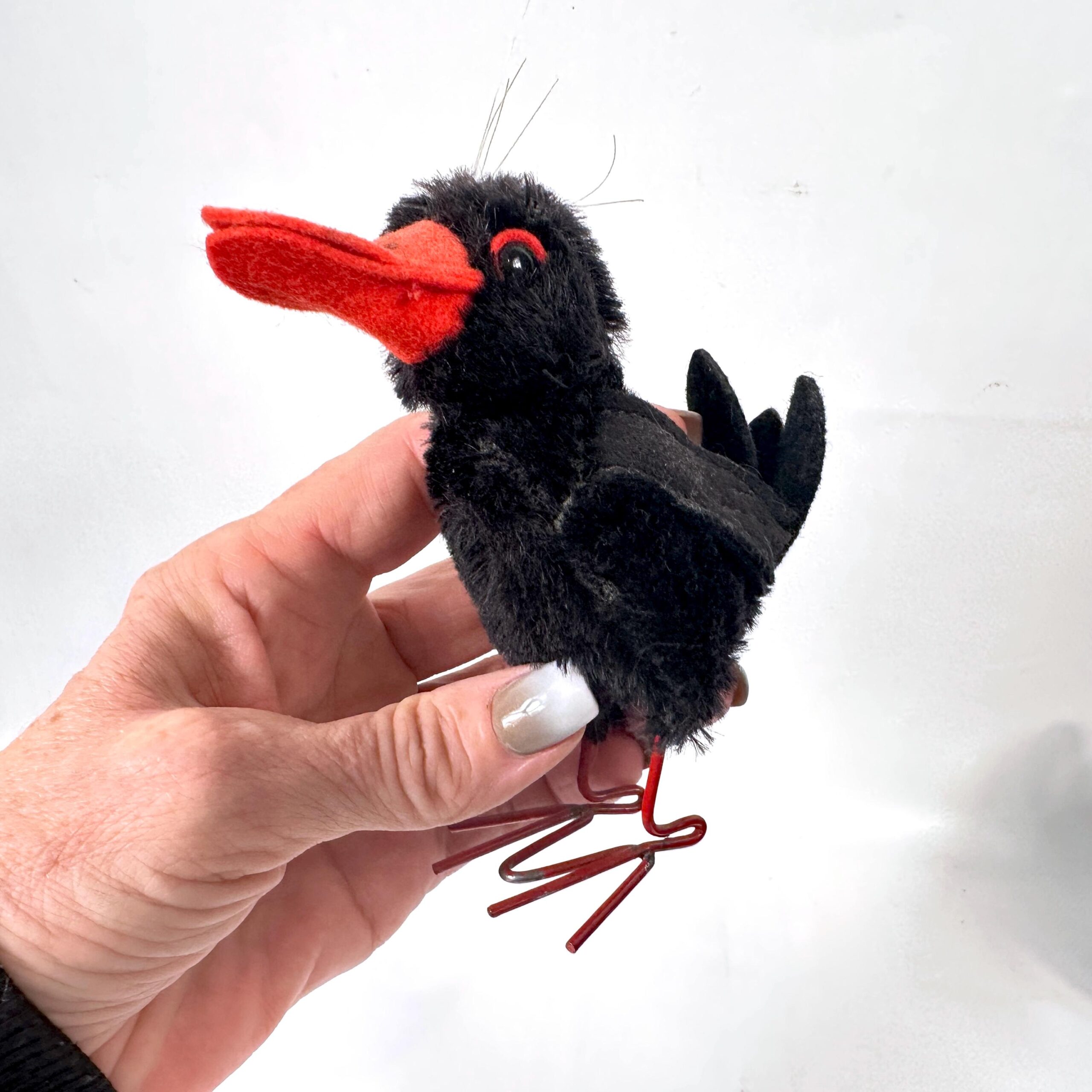 Vintage mohair bird in hand showing curved orange beak profile, jointed head mechanism, glass eye detail, and delicate wire l