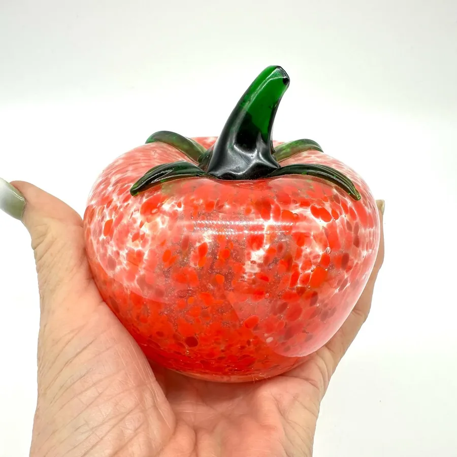 Vintage Murano-style hand-blown glass tomato with vibrant red body, white speckles, and green stem held in palm