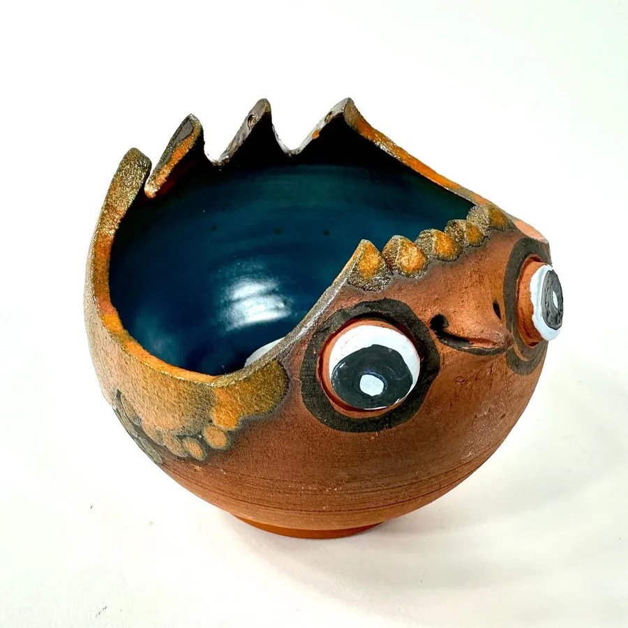 Vintage pottery bowl interior view showing deep blue glaze, pronounced eye features, and jagged rim design