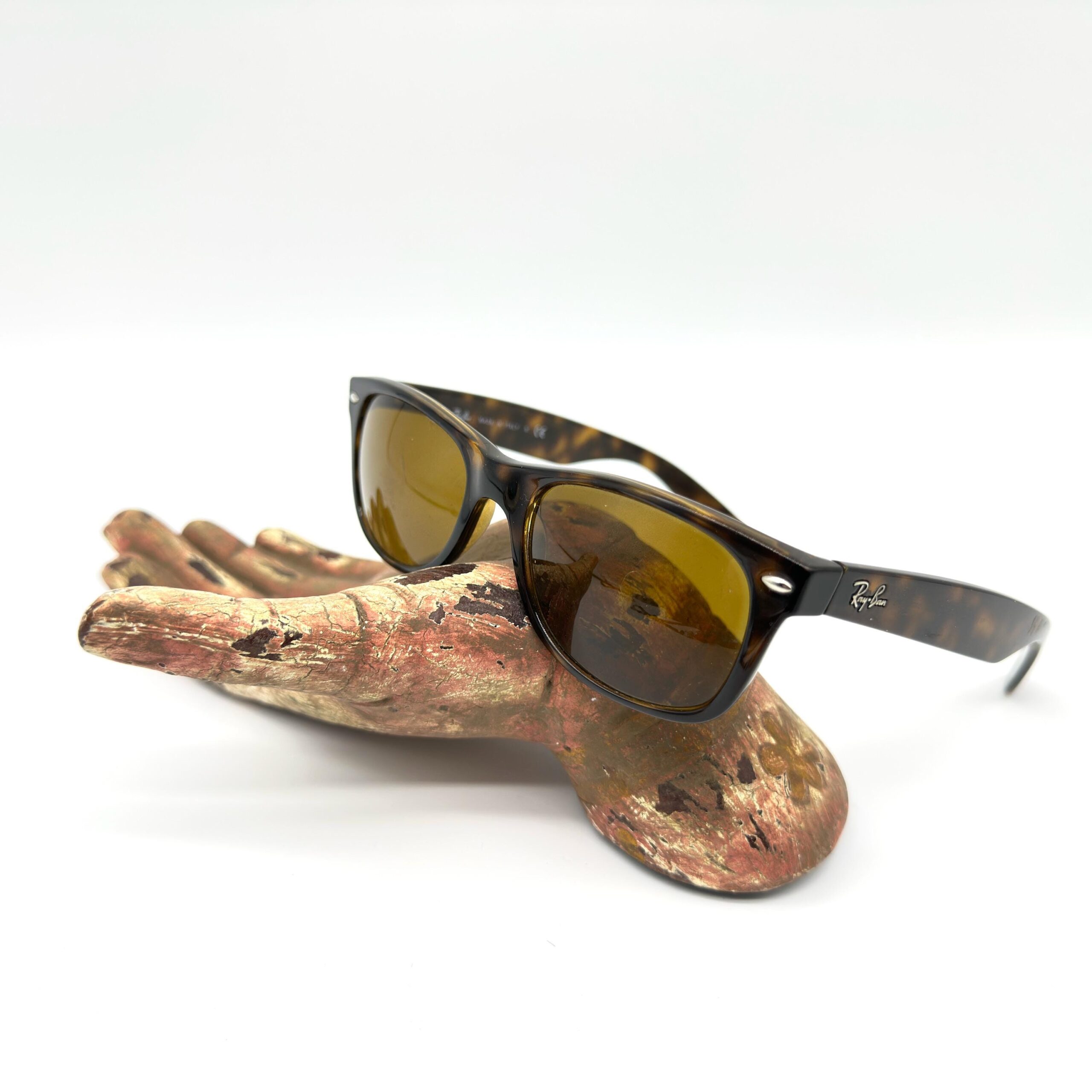 Vintage Ray-Ban Wayfarer RB2132 tortoiseshell sunglasses displayed on weathered driftwood, front three-quarter view