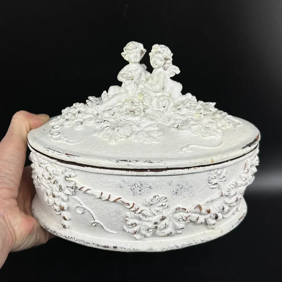 White hand-painted wooden cherub jewelry box with Rococo relief detailing and twin angel finial, shown in hand