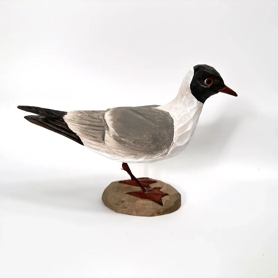Wooden seagull carving in resting position showing complete form, black wing tips, cream underside, and rustic base