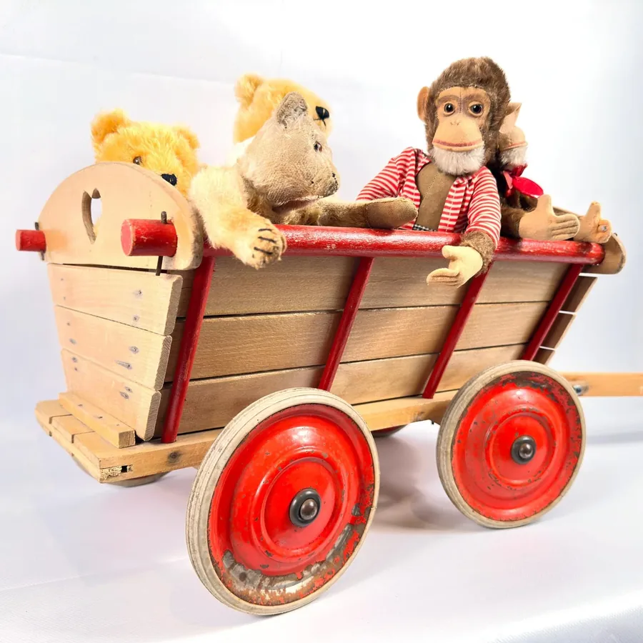 1940s wooden pull-along wagon with bright red metal wheels, natural wood body, and three vintage teddy bears seated inside