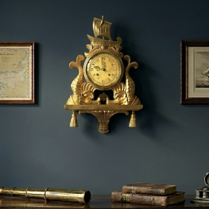 Ornate brass wall-mounted clock with decorative finials displayed against deep blue-grey painted wall