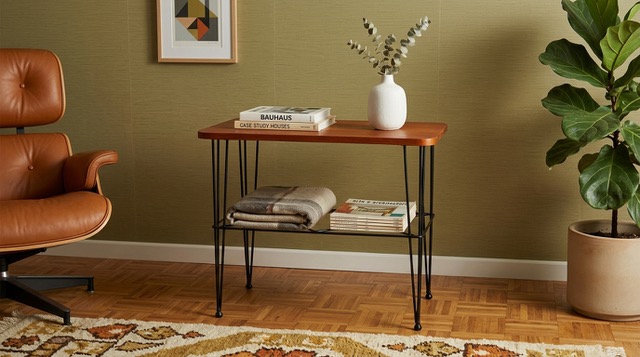 Mid-century side table with shelf storage in warm wood tones positioned against olive green wall