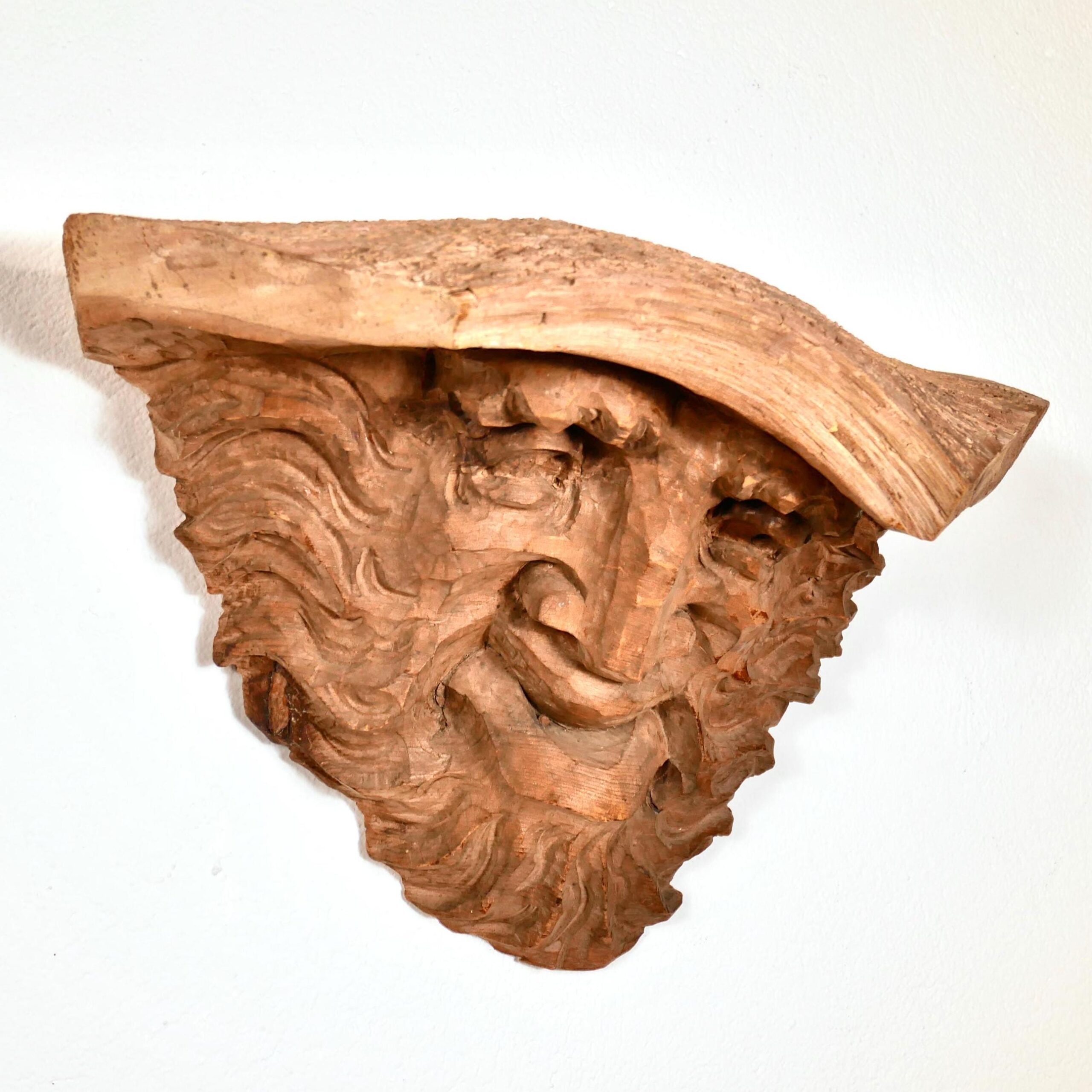 Angled side view of wooden sculpture highlighting the profile of carved nose, beard contours, and organic bark hat element