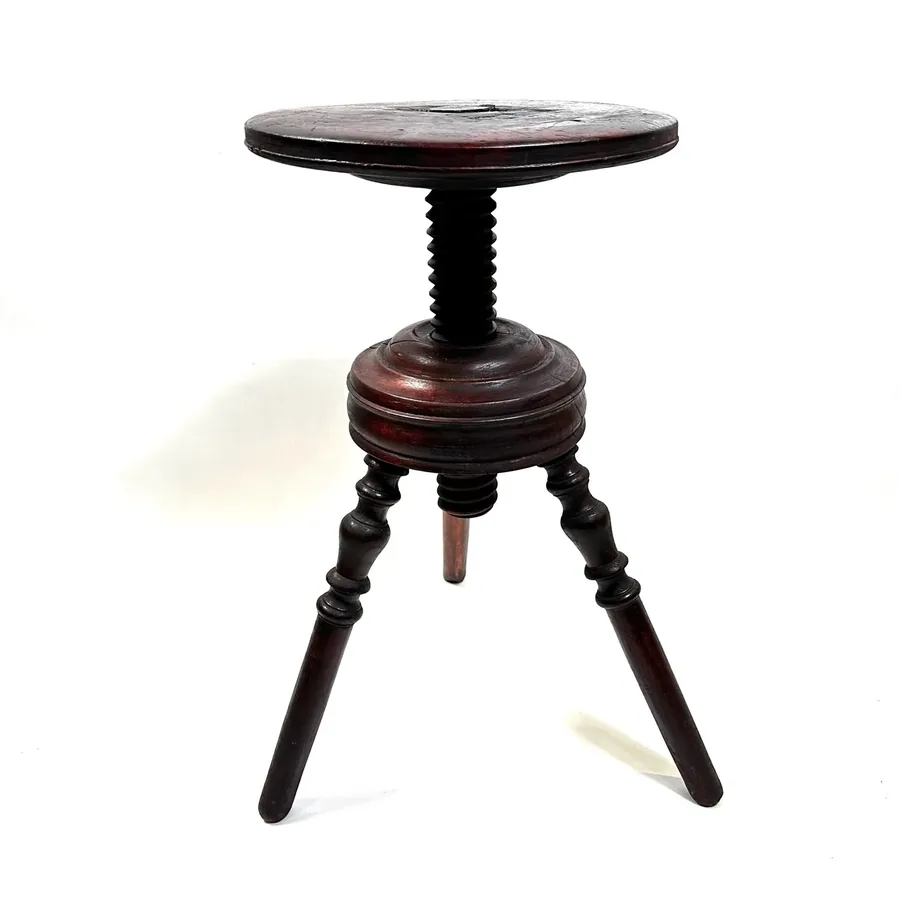 Antique wooden piano stool with round adjustable seat, turned wooden legs, and central screw mechanism, shown from front angl