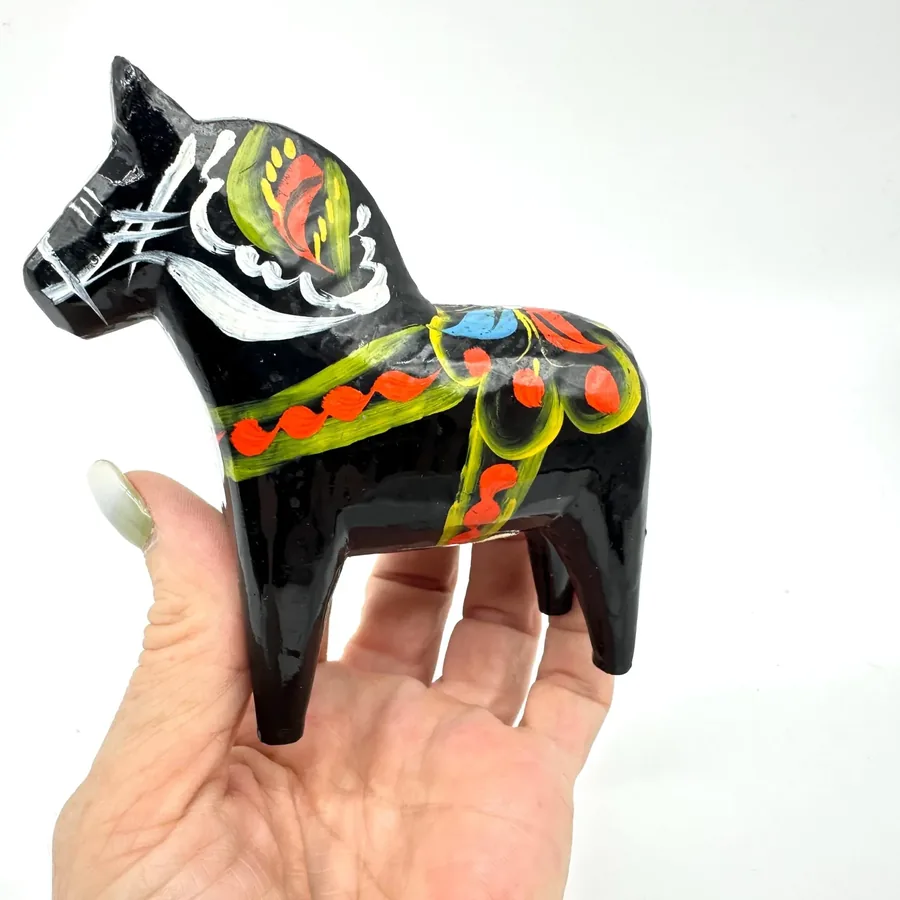 Black dala horse resting in hand, displaying hand-painted bridle and head detail with clear view of folk-art geometric color