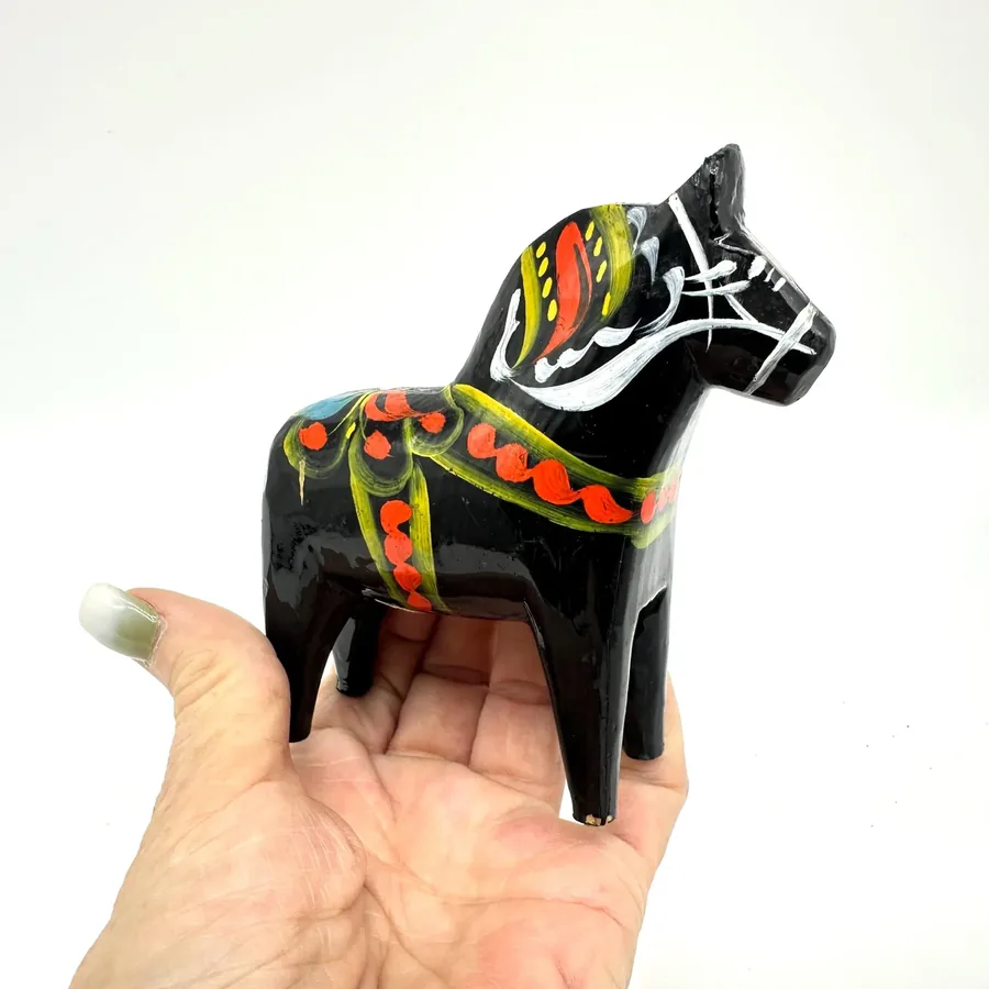 Black wooden dala horse in hand showing complete body profile with hand-painted multicolor saddle blanket and demonstrating t