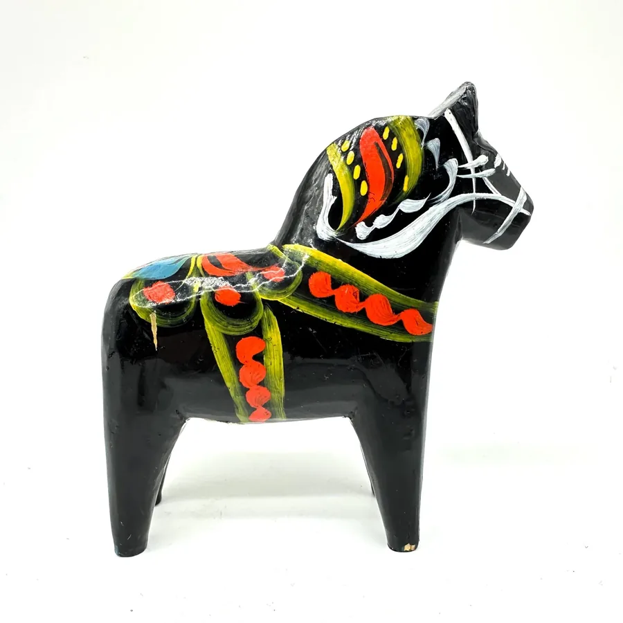 Black wooden dala horse with hand-painted multicolor textile pattern, showing three-quarter angle and side profile with disti