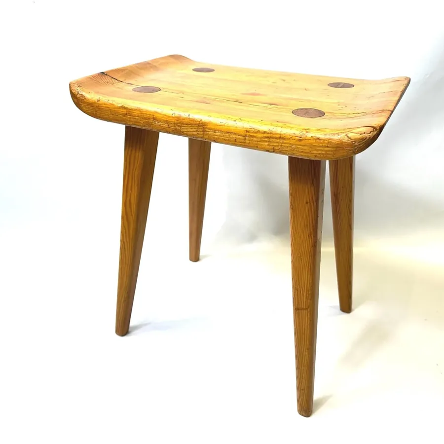 Carl Malmsten Visingsö pine saddle stool with tapered legs, front three-quarter view showing natural wood grain and curved se