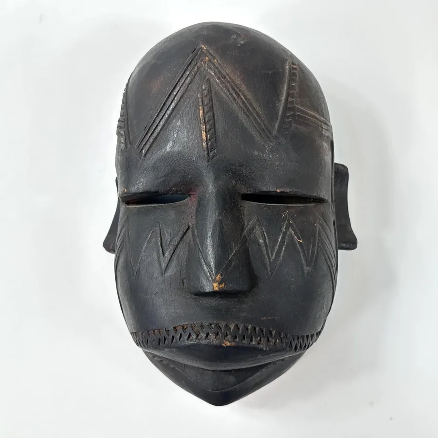 Direct frontal view of aged wooden mask, dark patina with carved facial features, geometric mouth design, prominent chin