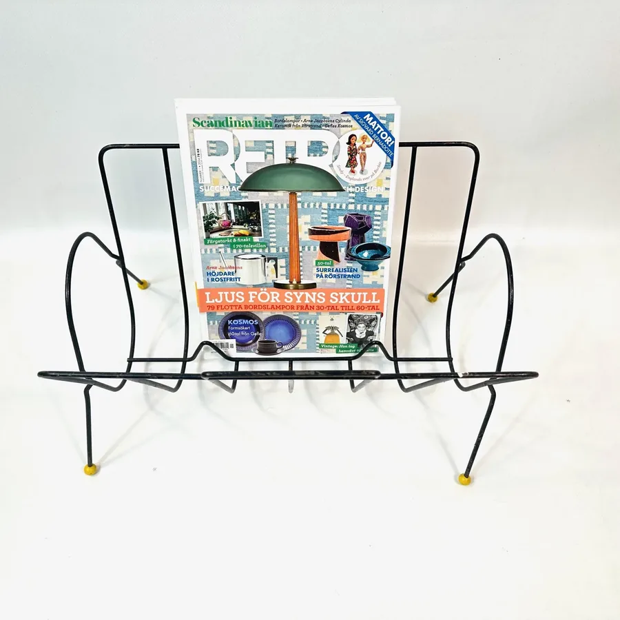 Front-centered view 1960s atomic wire rack with magazines showing black metal construction and yellow accent feet