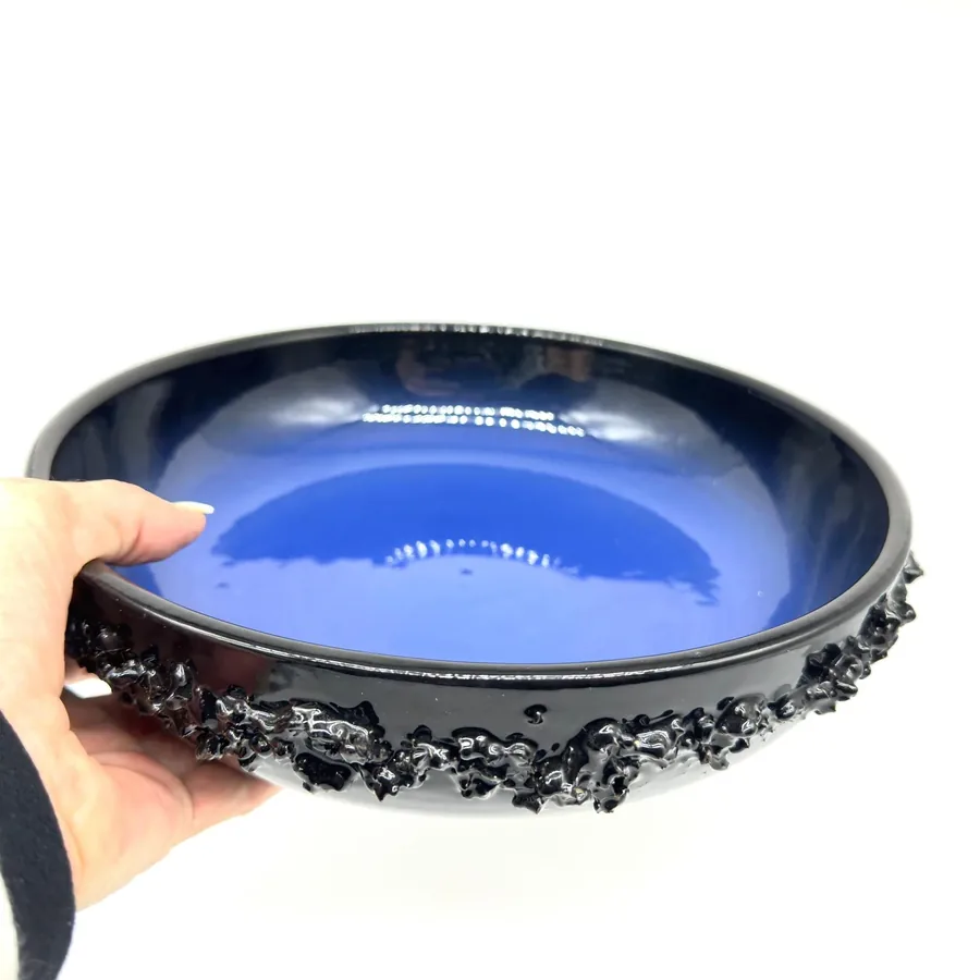 Glit Iceland lava glaze bowl held in hand, showing vibrant blue interior and textured black brutalist exterior from above