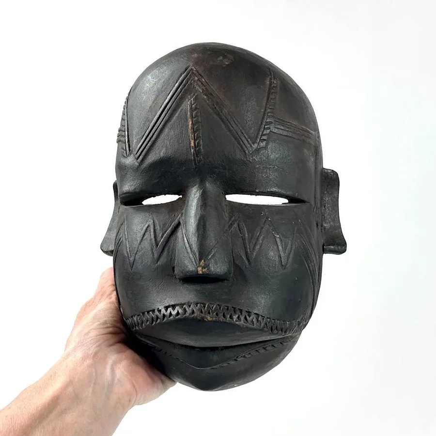 Hand-carved African tribal mask, dark wood with geometric diamond patterns, pronounced protruding features and striped mouth