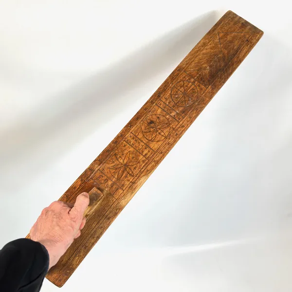 Hand holding Swedish mangling board, demonstrating scale and weight, aged honey-colored wood with visible patina