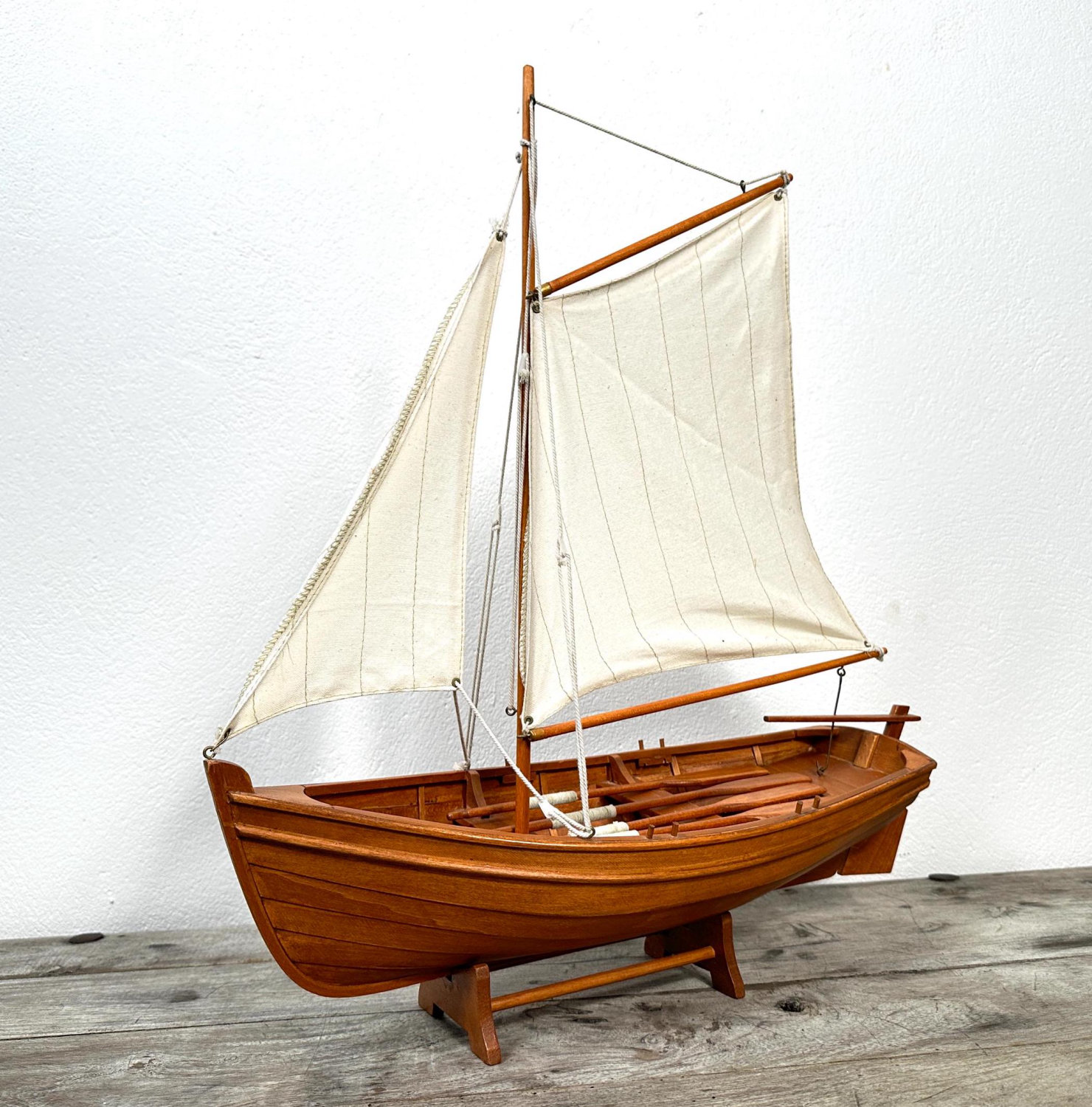 Handmade wooden sailboat model with natural wood hull, cream canvas sails, and wooden masts, displayed on gray surface