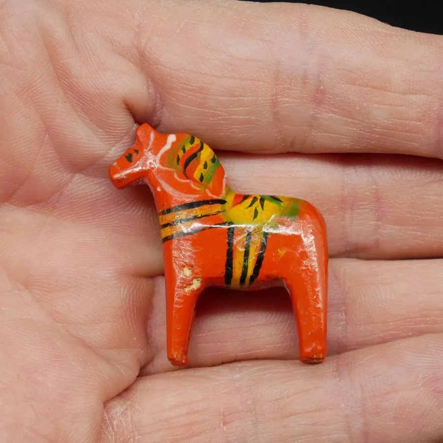 Horizontal palm view of red wood Dala horse miniature showing complete painted pattern, all four legs and carved proportions