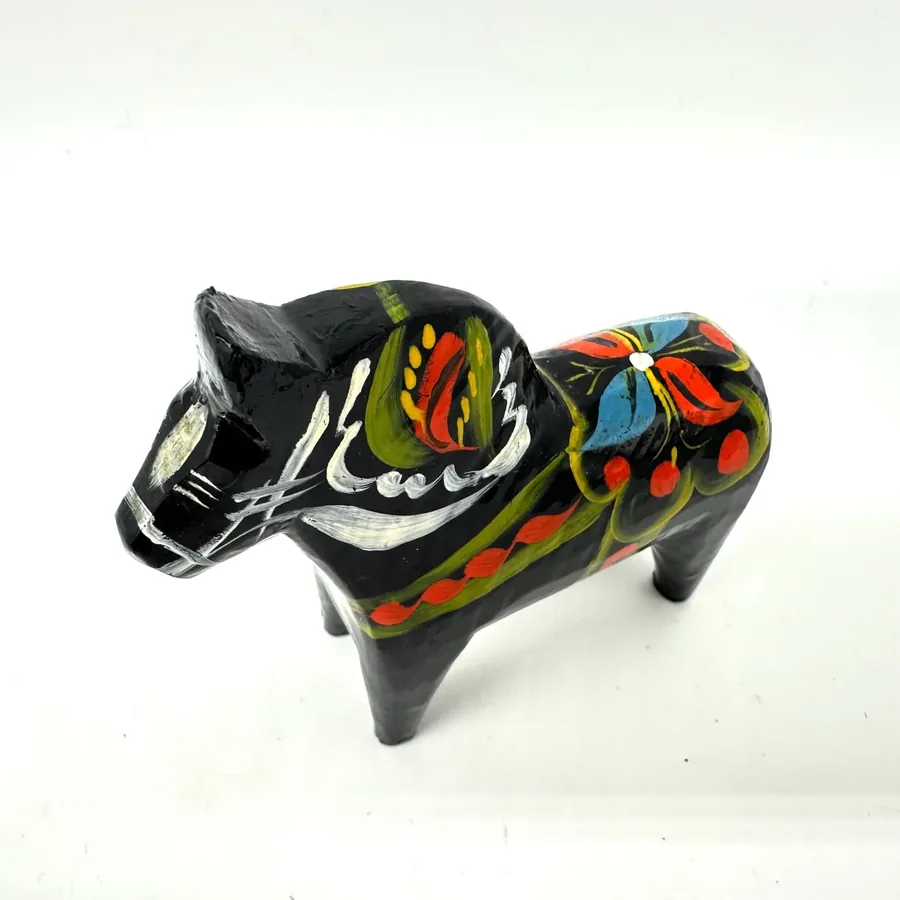 Horizontal perspective of black dala horse lying on side, revealing hand-painted textile patterns and showing the three-dimen