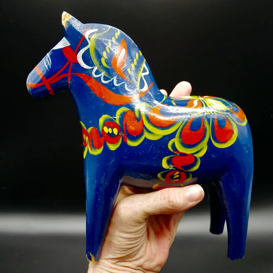 Large blue hand-painted Swedish Dala horse with vibrant red, orange, yellow folk art saddle design, held in palm