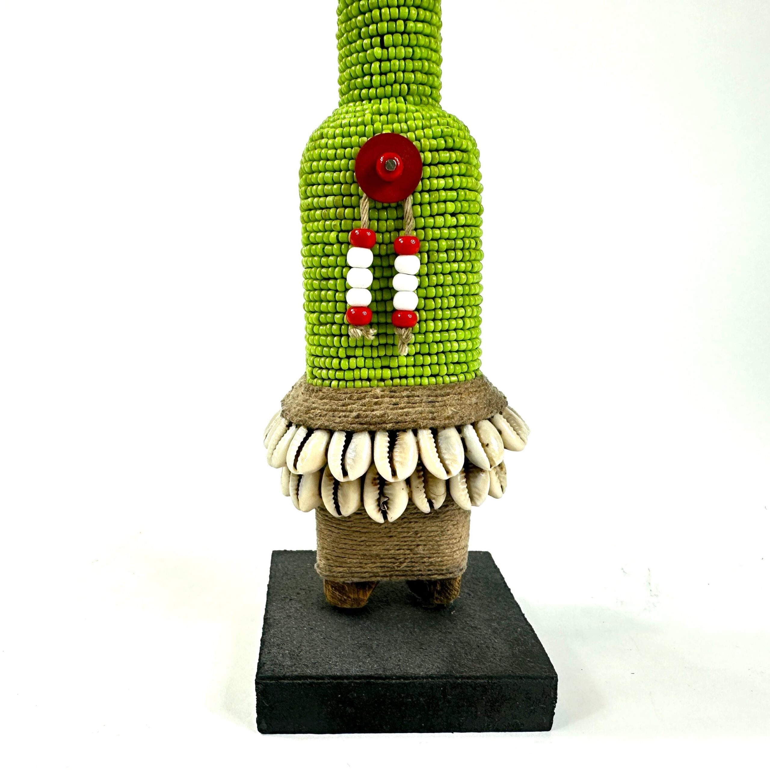 Lower portion of fertility doll emphasizing bright green beaded torso with red center motif, cream-colored cowrie shell skirt