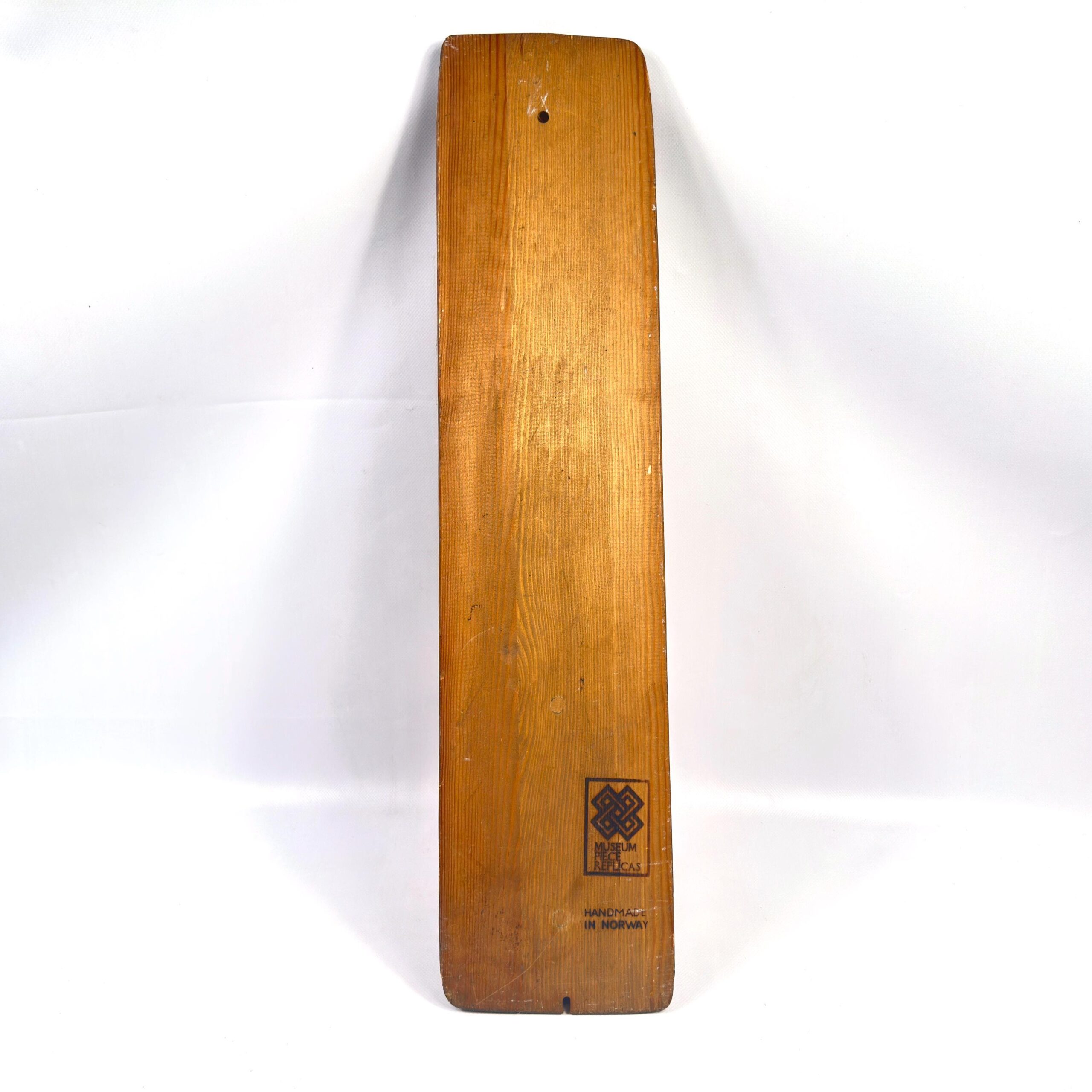Vertical hanging view of carved paddle displaying figure panel, handle proportions, and natural wood coloring