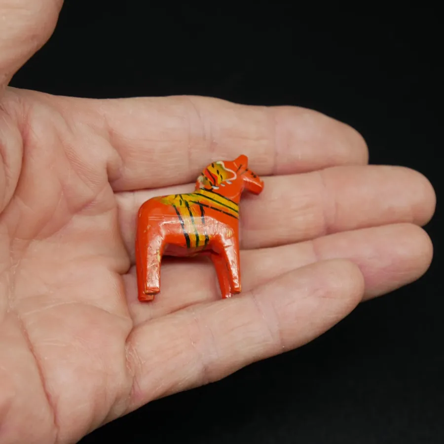 Miniature red Dala horse resting in open palm showing true scale and portable collectibility of this handmade wooden piece