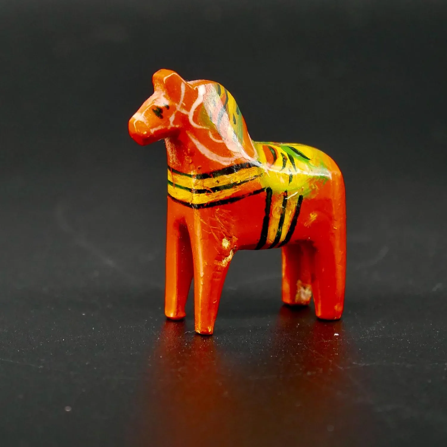 Miniature red Dala horse with hand-painted yellow and gold striped saddle, three-quarter front view showing carved wooden for