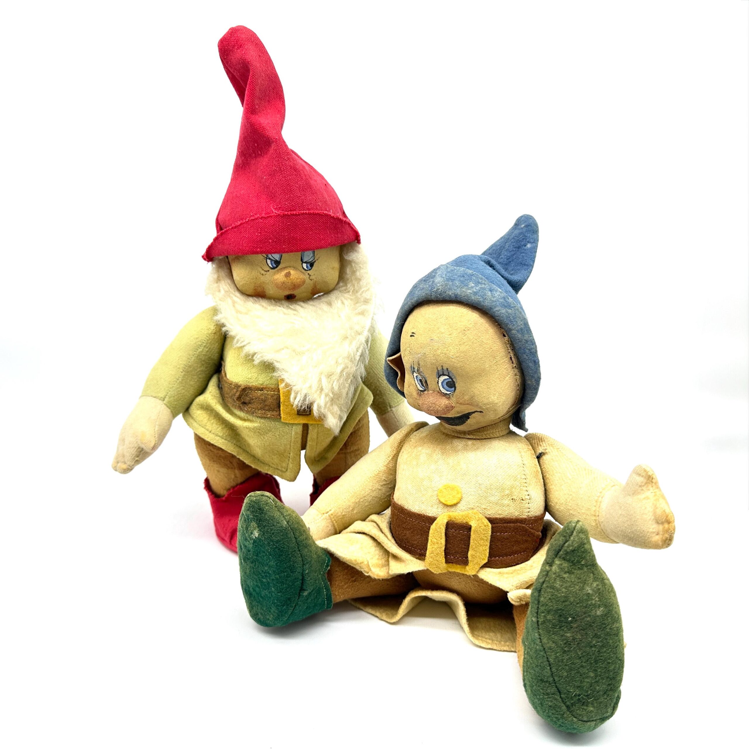 Pair of dwarf dolls together showing red-hatted figure with white beard and blue-hooded figure, both in yellow dresses with a