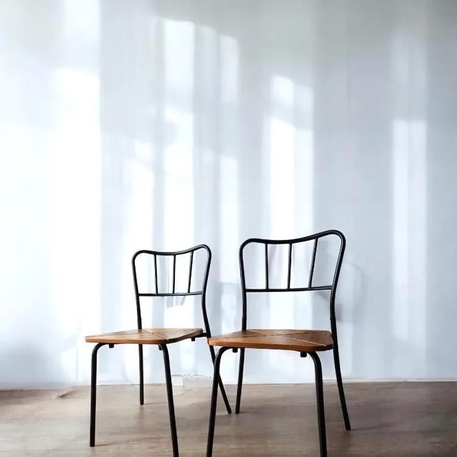 Pair of vintage IKEA Agne chairs with black metal frames and warm pine wood seats, angled view showing stackable design